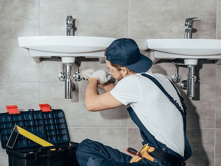 A man repairs a sink in a bathroom, showcasing plumbing services available in Denver, CO